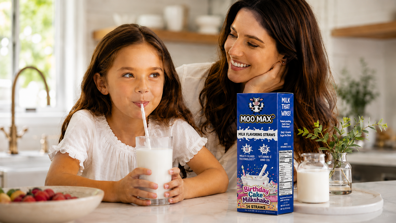 Child drinking milk through a MooMax Milk Flavoring Straw with a parent nearby and a MooMax Birthday Cake Milk Flavoring Straws box on the kitchen counter.
